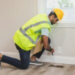 Construction worker conducting a home inspection indoors, using tools near a vent.
